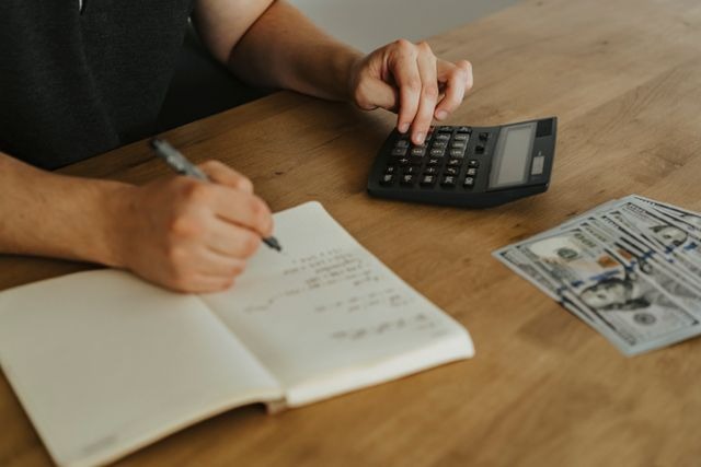 person taking notes while typing on a calculator