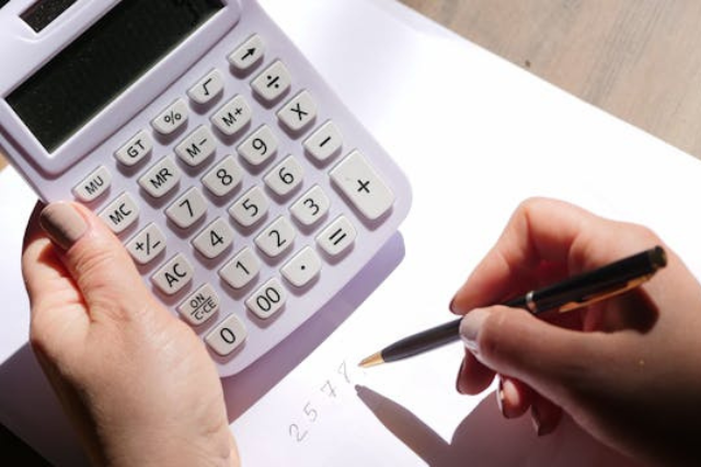 a-person-using-a-white-calculator-while-writing-numbers-on-a-sheet-of-paper-with-a-black-pen