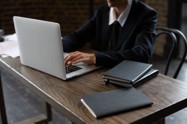 person in a suit typing on a laptop at a wooden desk